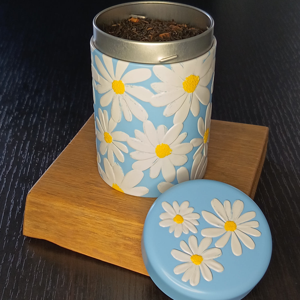 Boîte à thé Daisy bleue ouverte, couvercle retiré et feuilles de thé en vrac — Teavora