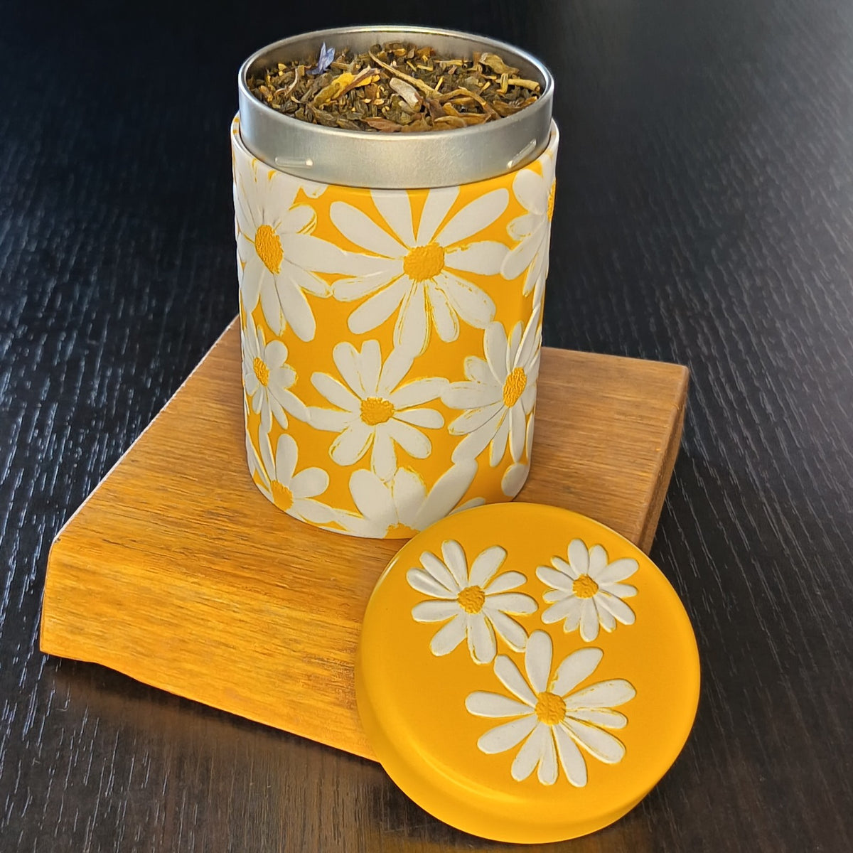 Boîte à thé Daisy jaune ouverte, couvercle retiré et feuilles de thé en vrac — Teavora