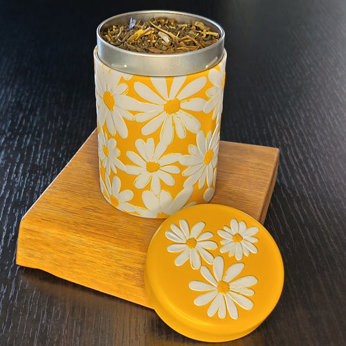 Boîte à thé Daisy jaune ouverte, couvercle retiré et feuilles de thé en vrac — Teavora