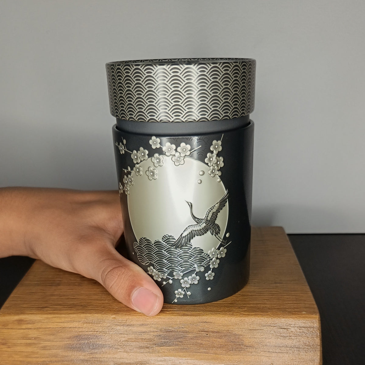 Boîte à thé en métal Komorebi noire 150 g tenue en main, taille réelle — Teavora